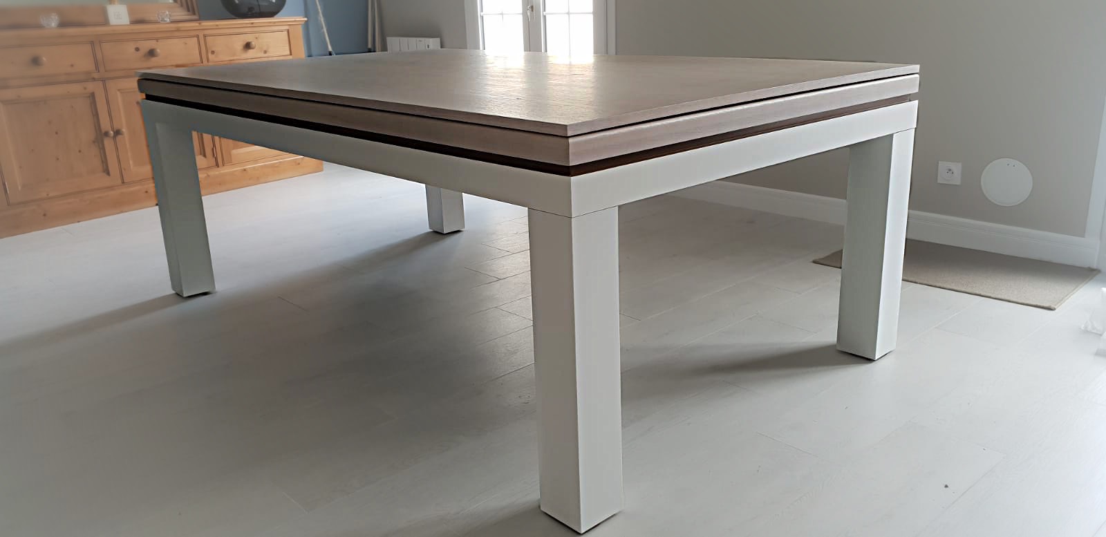 Billard-table design avec plateau en chêne sur pied blanc séparé par un liseré sombre.